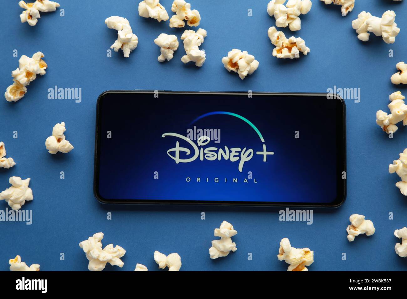 Nikolaev, Ukraine - 20 novembre 2021. Films et séries par abonnement, concept. Smartphone avec logo Disney plus et pop-corn sur fond bleu. À Banque D'Images