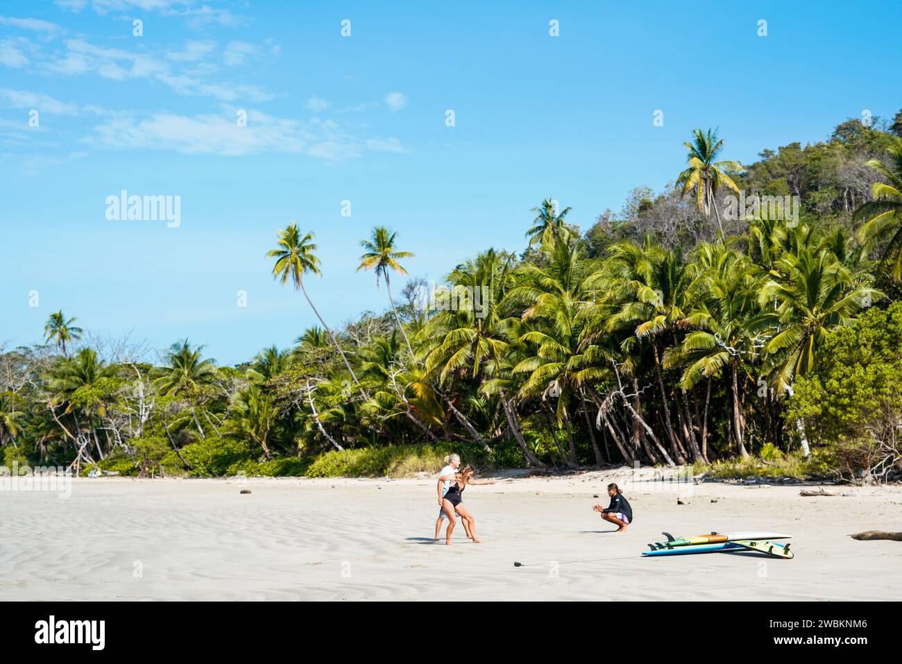 Instructeur de surf avec des étudiants d'âge moyen sur une plage tropicale de sable blanc apprenant à surfer avec trois planches de surf à côté d'eux. Banque D'Images