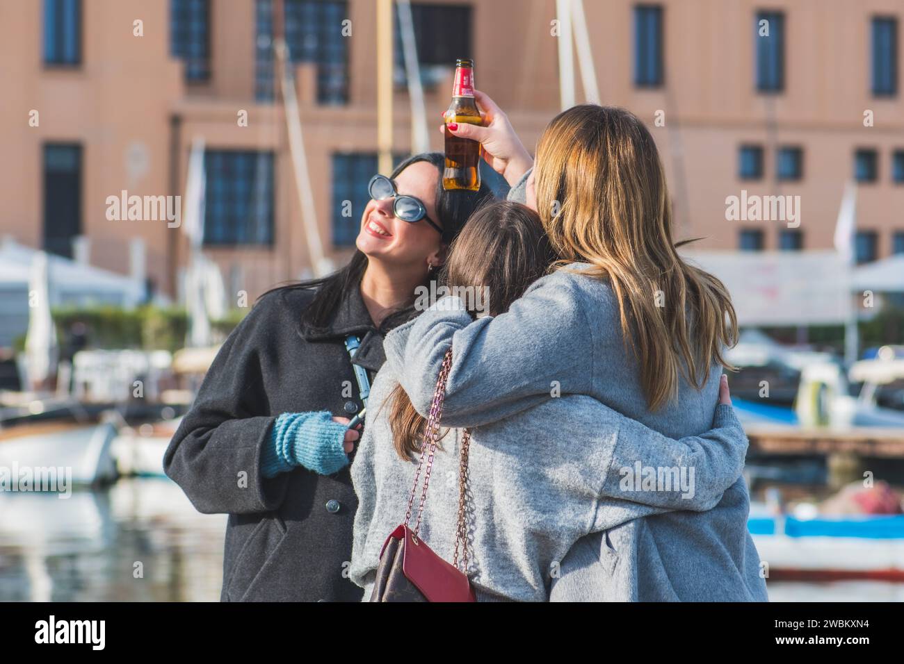 Belles jeunes filles buvant de la bière et s'amusant sur la jetée du petit port de Bari, Pouilles, Italie avec des bateaux et du théâtre en arrière-plan Banque D'Images