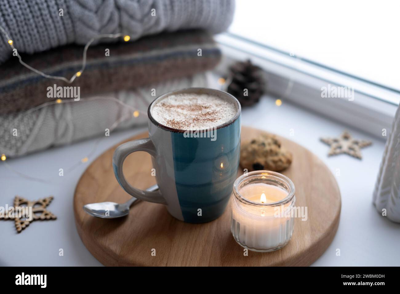 Nature morte de rebord de fenêtre d'hiver. Tasse en céramique bleue de café chaud sur le rebord de la fenêtre. Décorations de Noël sur le fond. Image de la maison confortable. Woolen k chaud Banque D'Images