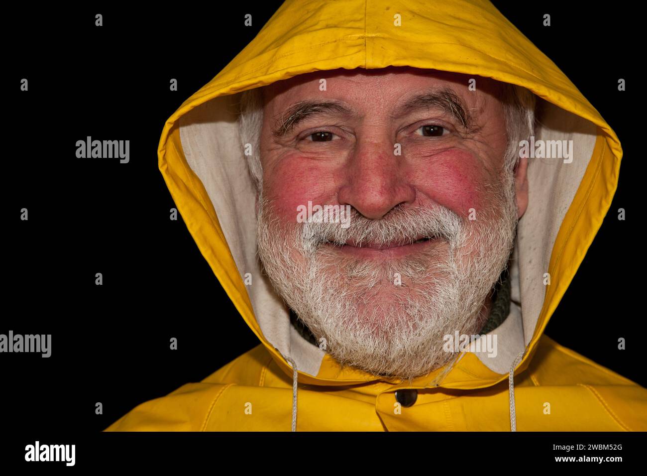 Un marin à la retraite, souriant brillamment et plein de joie sous son capot jaune, prêt pour la prochaine aventure sur terre ferme! Banque D'Images