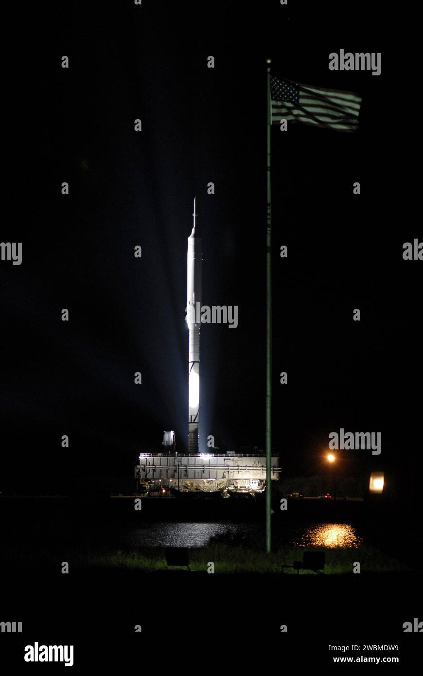 Alors que la fusée Ares I-X se déplace vers le Launch Pad 39B au sommet d'un transporteur à chenilles au Kennedy Space Center, le drapeau américain agite à proximité. Le déploiement de la fusée sur 4,2 milles fait partie des préparatifs du programme Constellation pour le vol d’essai Ares I le 27 octobre. Banque D'Images