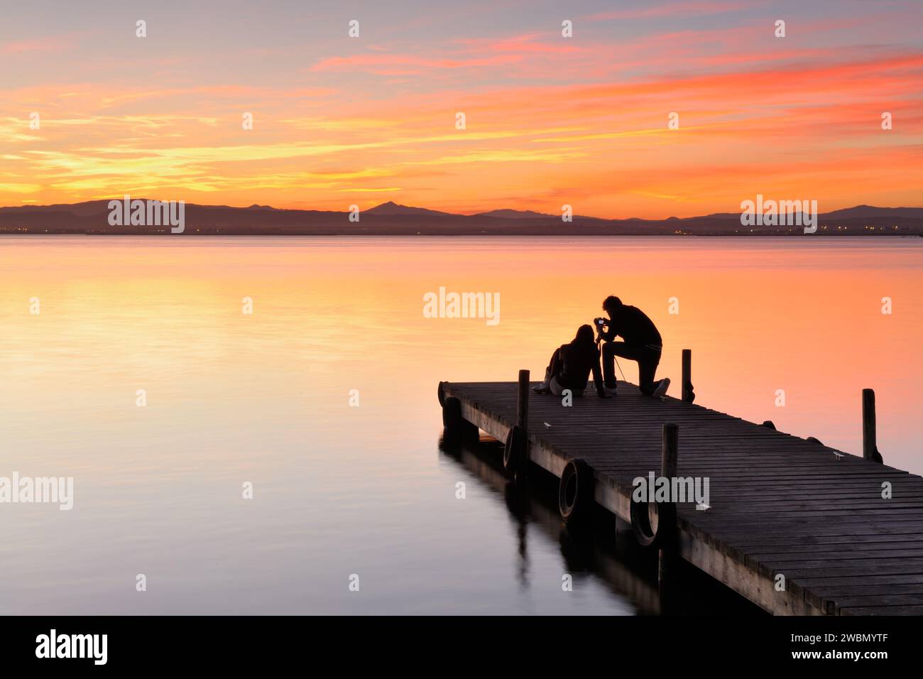 Silhouettes rétroéclairées de deux personnes prenant des photos d'un magnifique coucher de soleil sur la passerelle du lac Albufera à Valence, en Espagne. Banque D'Images