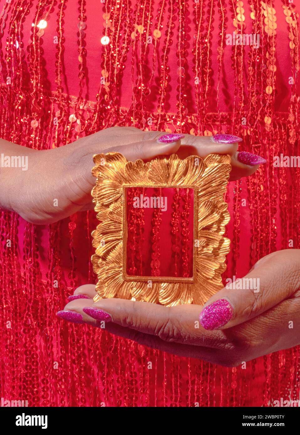 Une femme afro-américaine diversifiée vêtue de sequins rouges et portant un vernis à ongles rose tenant un cadre en or Banque D'Images