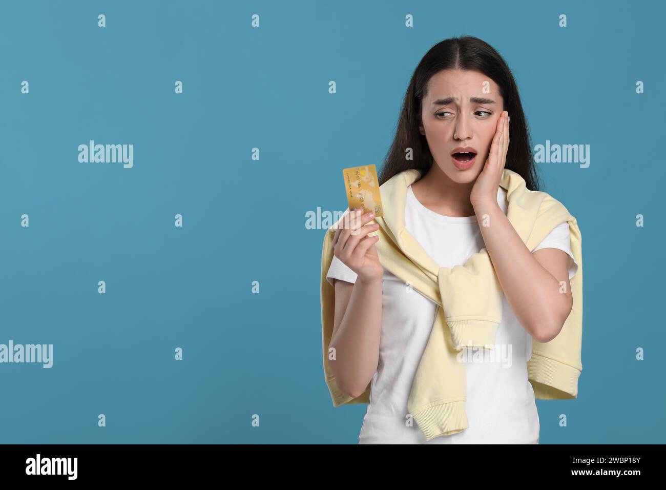 Femme choquée avec carte de crédit sur fond bleu clair, espace pour le texte. Problème de dette Banque D'Images