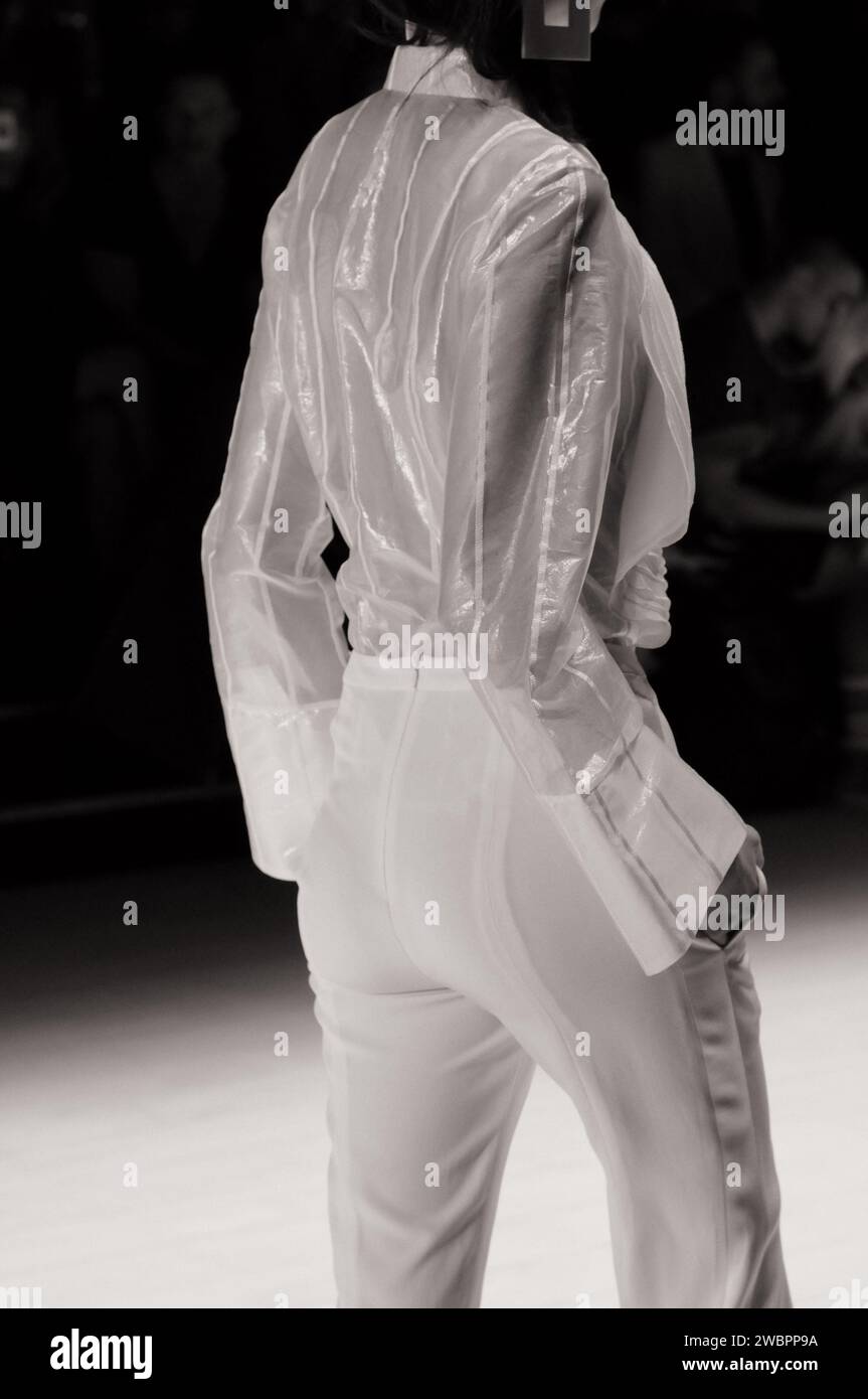 Mannequin portant un chemisier à manches longues blanc transparent avec des rayures blanches et un pantalon blanc vu de derrière au Raffles Graduate Runway Fashion Show Banque D'Images