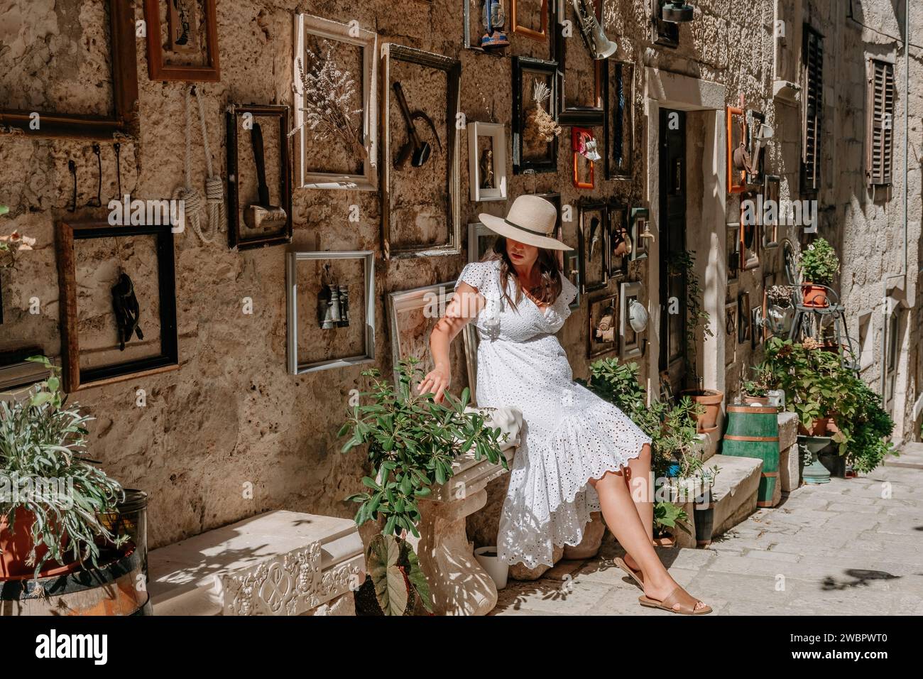 Une femme élégante enfilant une robe blanche immaculée et un chapeau se relaxant dans une ruelle pittoresque Banque D'Images