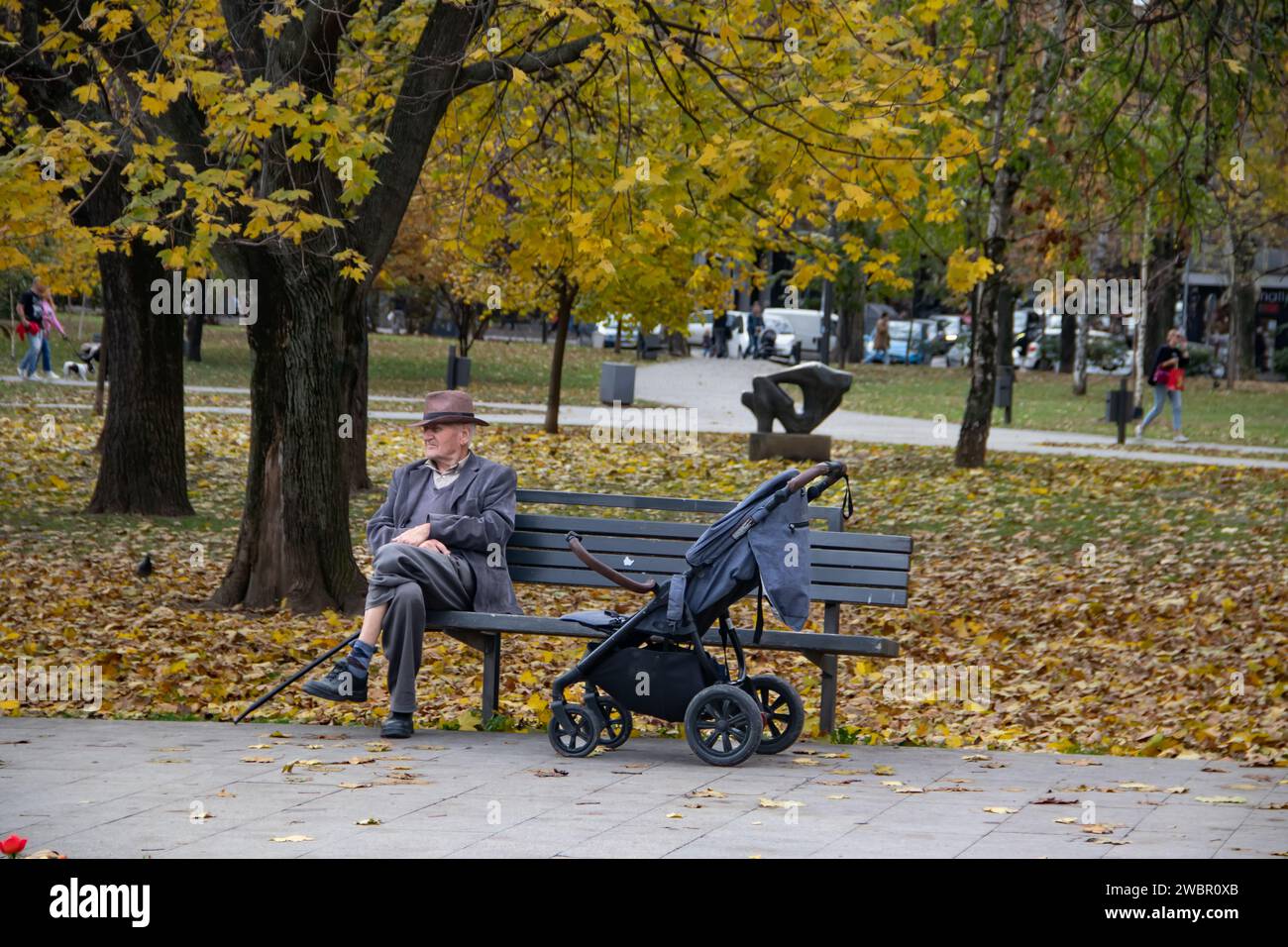 Grand-père prenant petit-enfant pour une promenade reposant sur le banc dans le parc public de la ville Banque D'Images