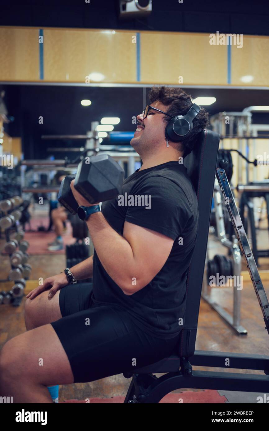Homme souriant effectue la formation de poids dans une salle de gym Banque D'Images