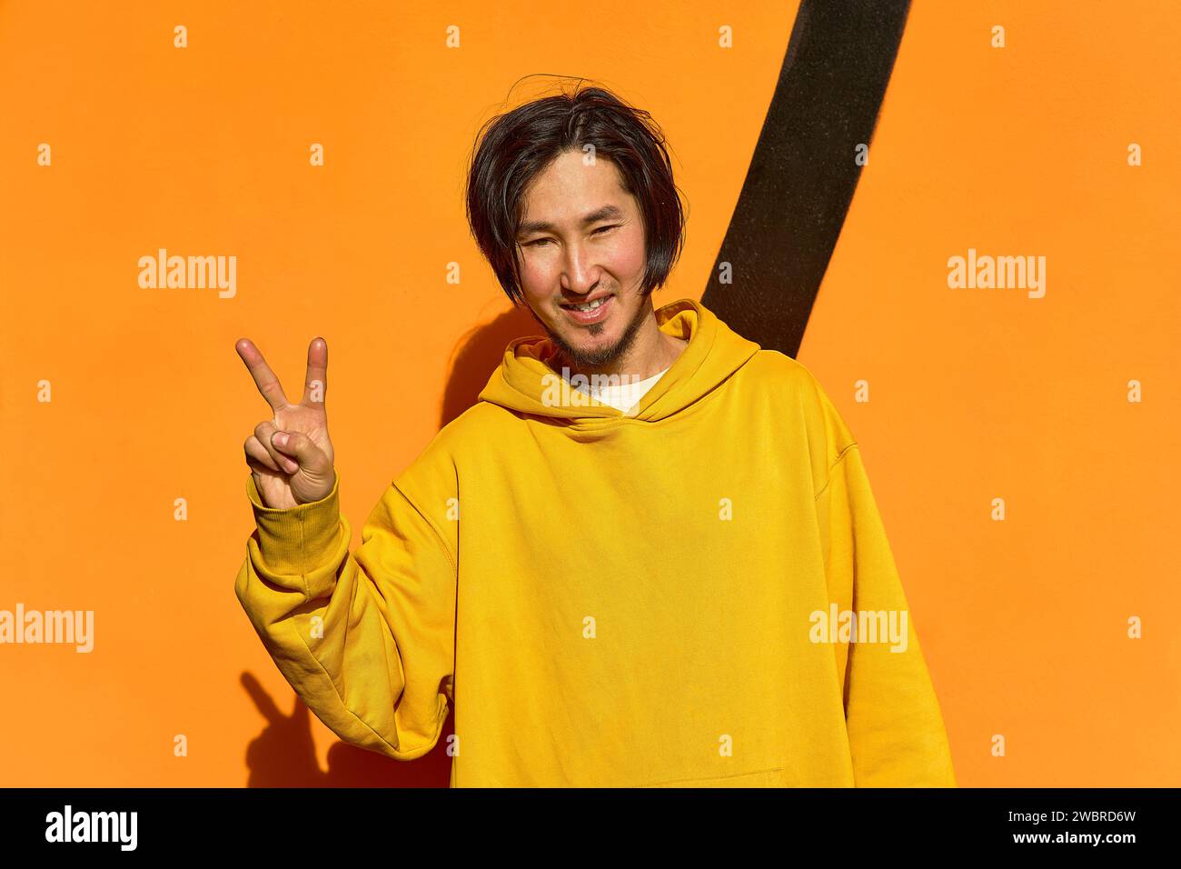 Un homme asiatique dans un sweat à capuche jaune se tient debout et montre un geste de paix, un Banque D'Images