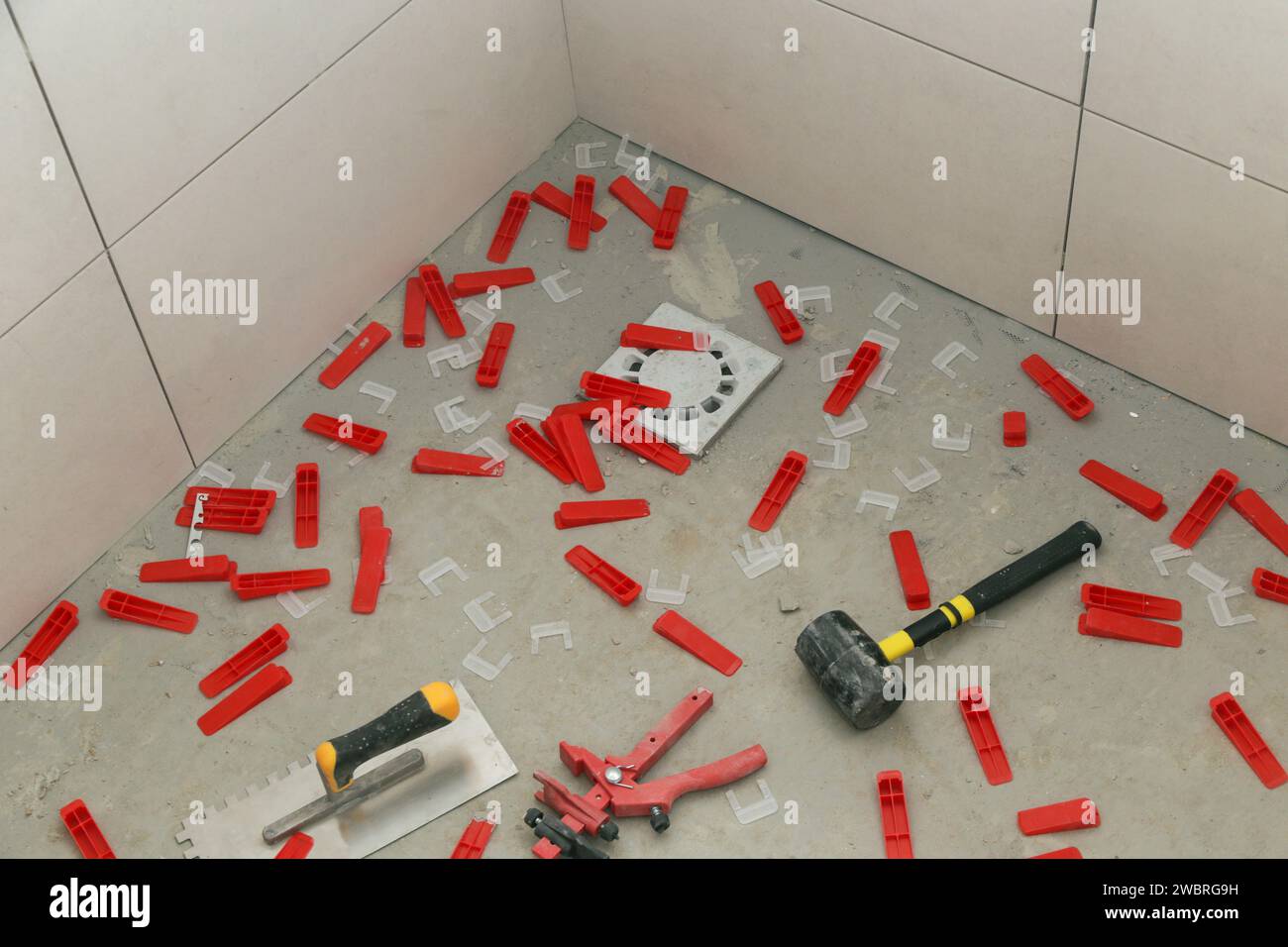 Système de nivellement de carreaux en plastique, truelle crantée et marteau en caoutchouc pour carreaux sur le sol. Processus d'installation de carreaux dans la salle de bain. Impr. Maison bricolage Banque D'Images