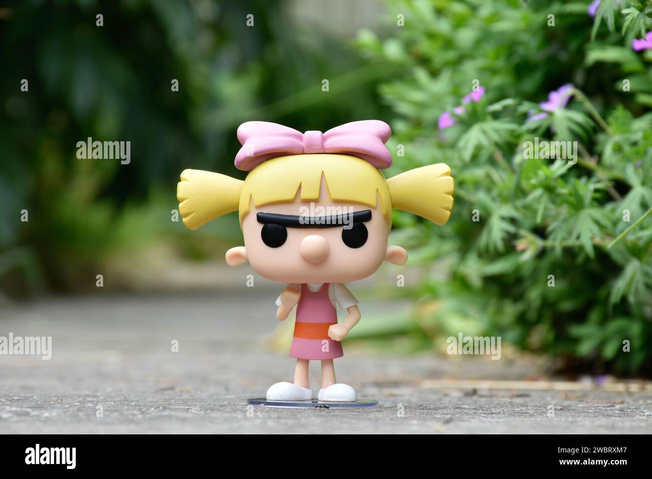 Funko Pop figurine d'action de Helga Pataki de la série télévisée d'animation Nickelodeon Hey Arnold. Jouet debout sur la route asphaltée dans le parc de printemps, fleurs roses. Banque D'Images