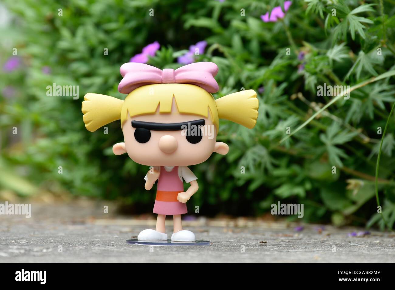 Funko Pop figurine d'action de Helga Pataki de la série télévisée d'animation Nickelodeon Hey Arnold. Jouet debout sur la route asphaltée dans le parc de printemps, fleurs roses. Banque D'Images