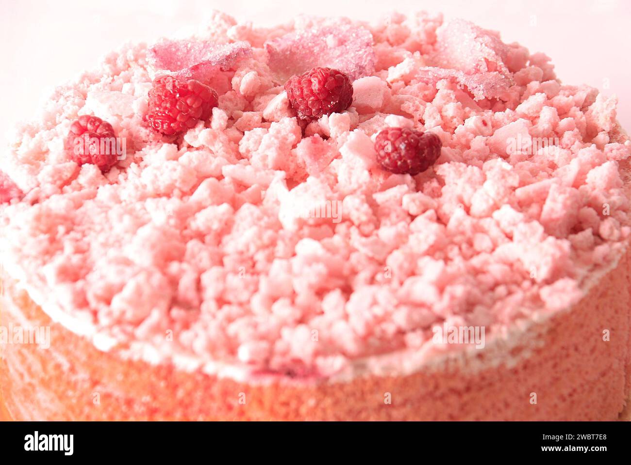 Un gâteau rose recouvert de meringue charlottes, framboises et pétales de rose sucrés. Banque D'Images