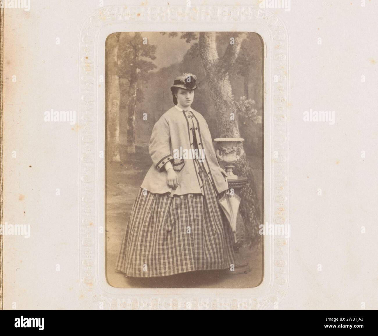 Portrait d'une femme avec chapeau, manteau et parapluie, debout près d'une colonne avec vase, anonyme, 1860 - 1900 Photographie. Carte de visite cette photo fait partie d'un album. Carton néerlandais. Support photographique albumen print personnes historiques - BB - femme. Figure debout - AA - figure humaine féminine. parapluie. piédestal d'un morceau de sculpture (peut-être sous la forme d'un herm) Banque D'Images