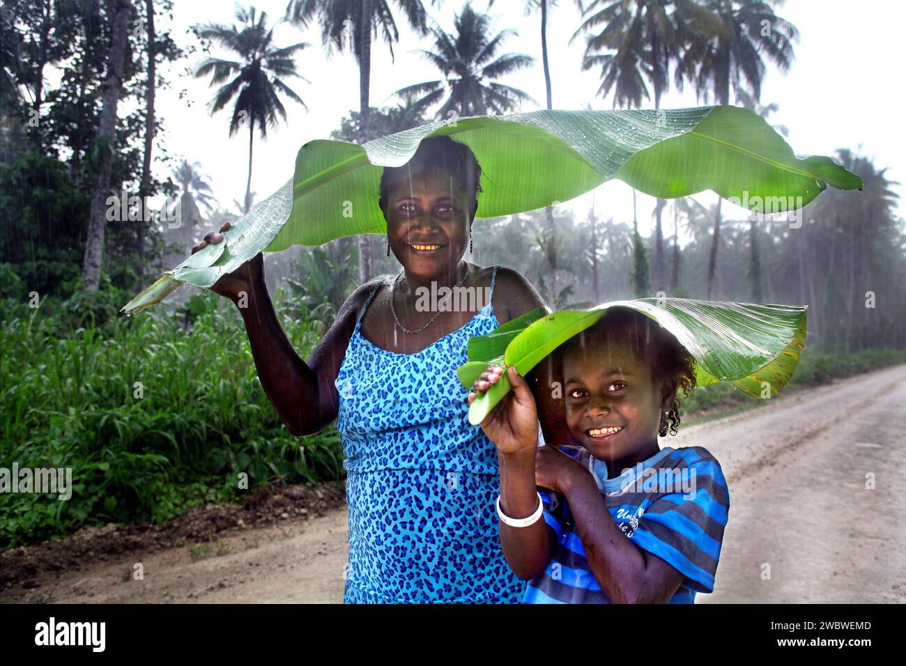 Mère et sa fille se protègent de la pluie avec un parapluie fait de feuilles de bananier. Région autonome de Bougainville, Papouasie-Nouvelle-Guinée, Asie Banque D'Images