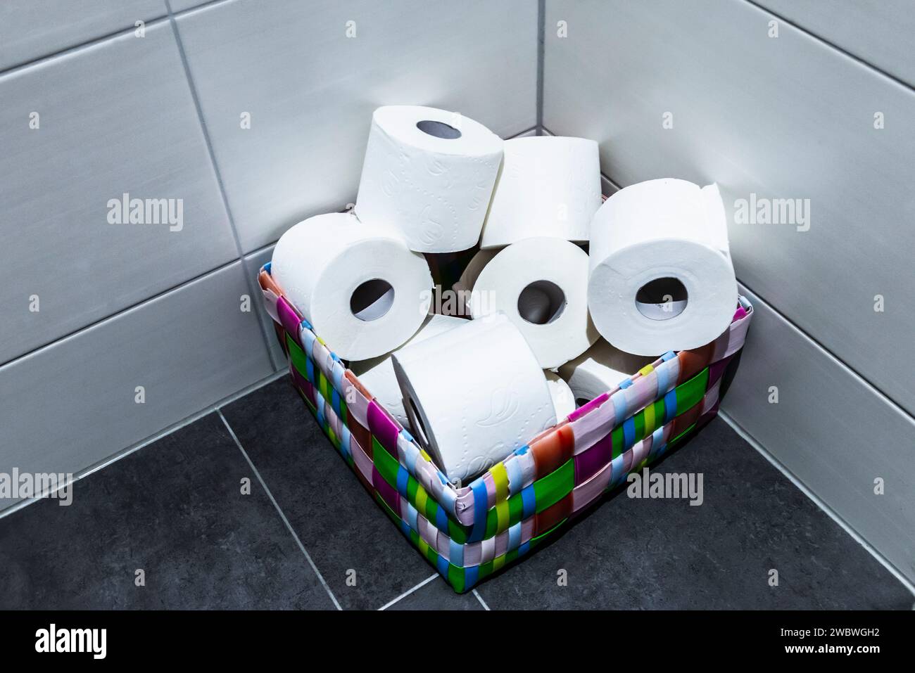 Une pile de rouleaux de papier toilette dans un panier coloré dans le coin d'une toilette ou d'une toilette Banque D'Images Une pile de rouleaux de papier toilette dans un panier coloré dans le coin d'une toilette ou d'une toilette Banque D'Images