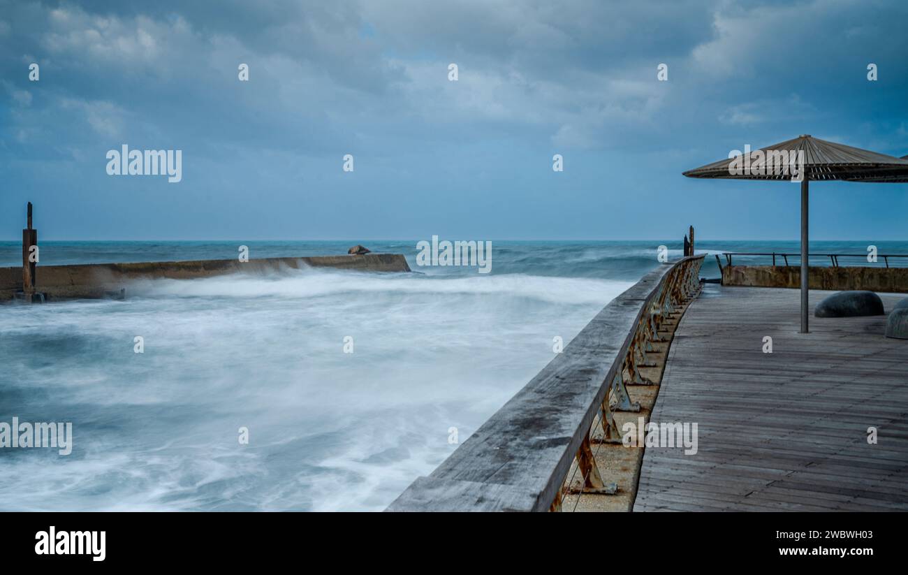 Une promenade en bois pittoresque ornée d'un parapluie vibrant, offrant de l'ombre et ajoutant une touche de couleur sur fond d'une vue sereine sur l'océan Banque D'Images