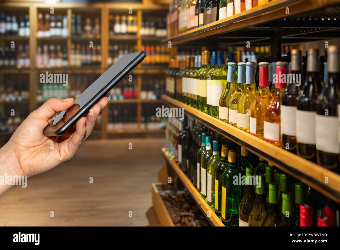 Téléphone portable dans la main féminine dans les bouteilles de vin avant dans le magasin d'alcool. Informations numériques sur les vins et les produits alcoolisés. Banque D'Images