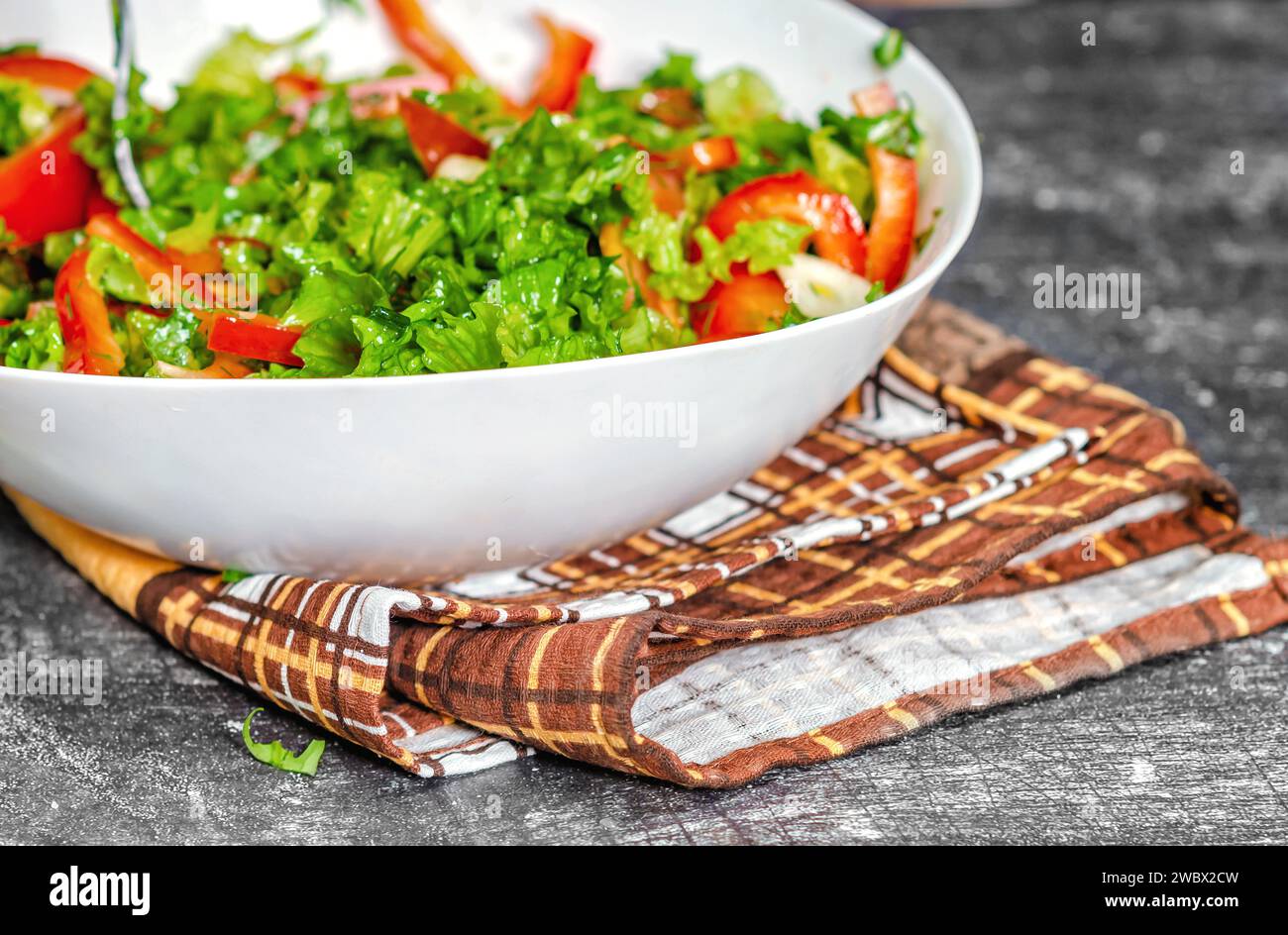 Gros plan d'un bol blanc délicieuse salade de légumes debout sur un torchon brun. Fond gris Banque D'Images
