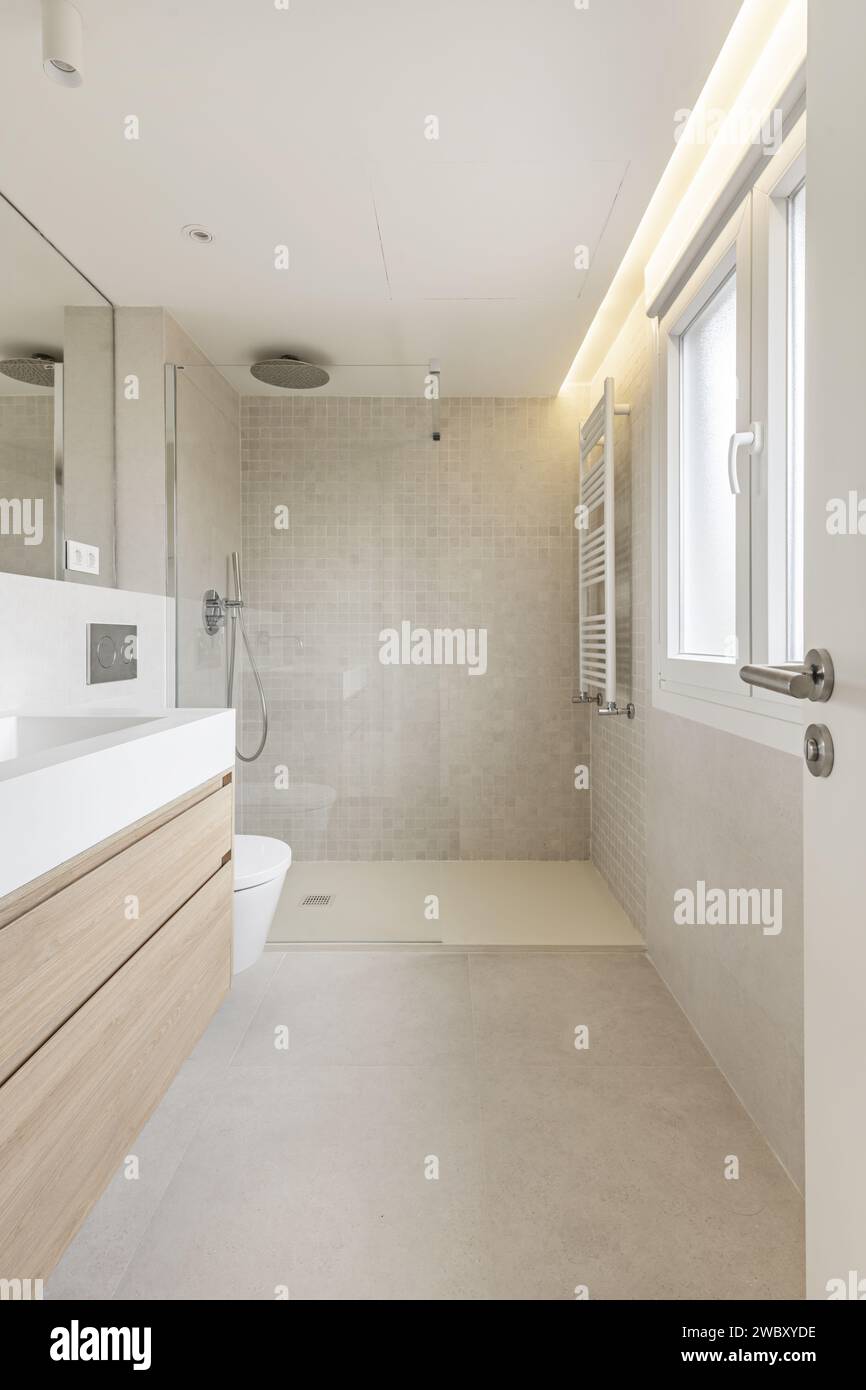 Salle de bain avec murs carrelés effet marbre, miroir mural intégré, sol en grès mat lisse, cabine de douche en verre trempé et porte-serviettes Banque D'Images