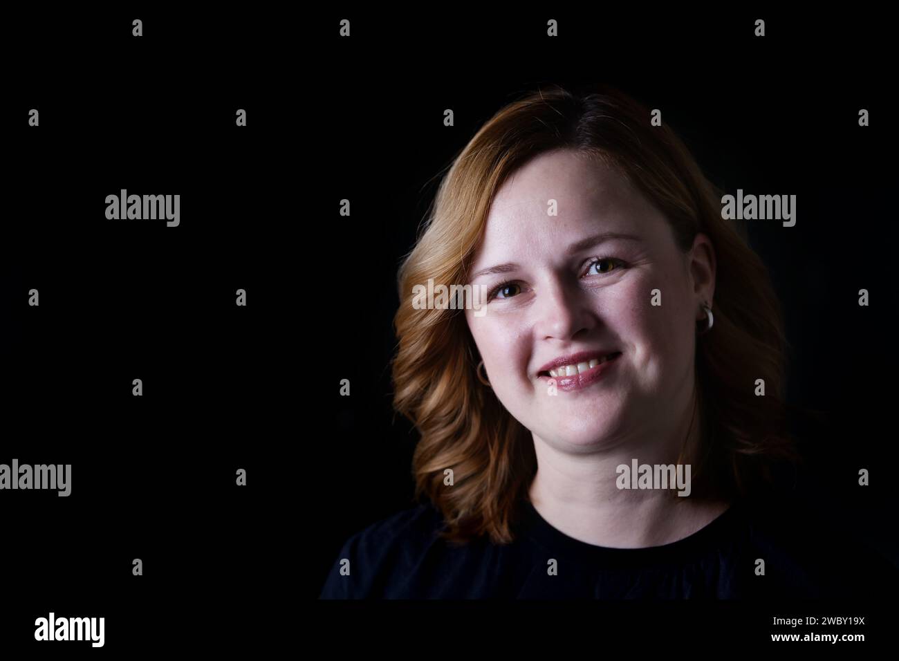 Portrait de belle femme souriante heureuse sur fond noir foncé. Gros plan portrait d'une femme blanche heureuse en basse tonalité. Copier l'espace pour le texte. Banque D'Images