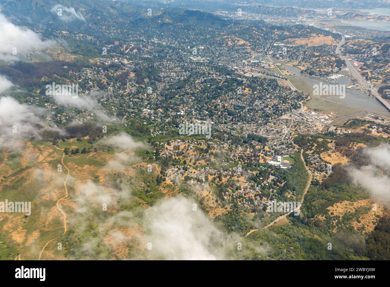 Une vue aérienne montre une ville nichée entre des collines vallonnées et une baie, partiellement obscurcie par des nuages, capturant le paysage urbain à la rencontre du terrain naturel. Banque D'Images