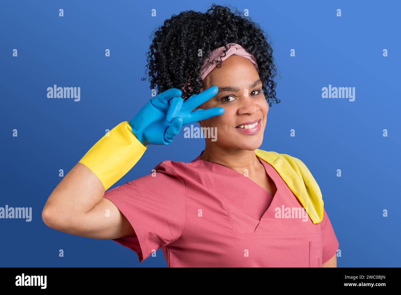 Heureux afro latina femme de nettoyage 40s pendant le nettoyage de printemps faisant un geste amical, isolé sur fond bleu Banque D'Images