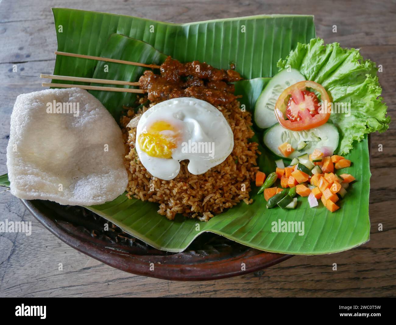 Riz frit ou Nasi Goreng indonésien servi sur une feuille de banane avec satay de poulet, œuf frit et cornichons. Banque D'Images