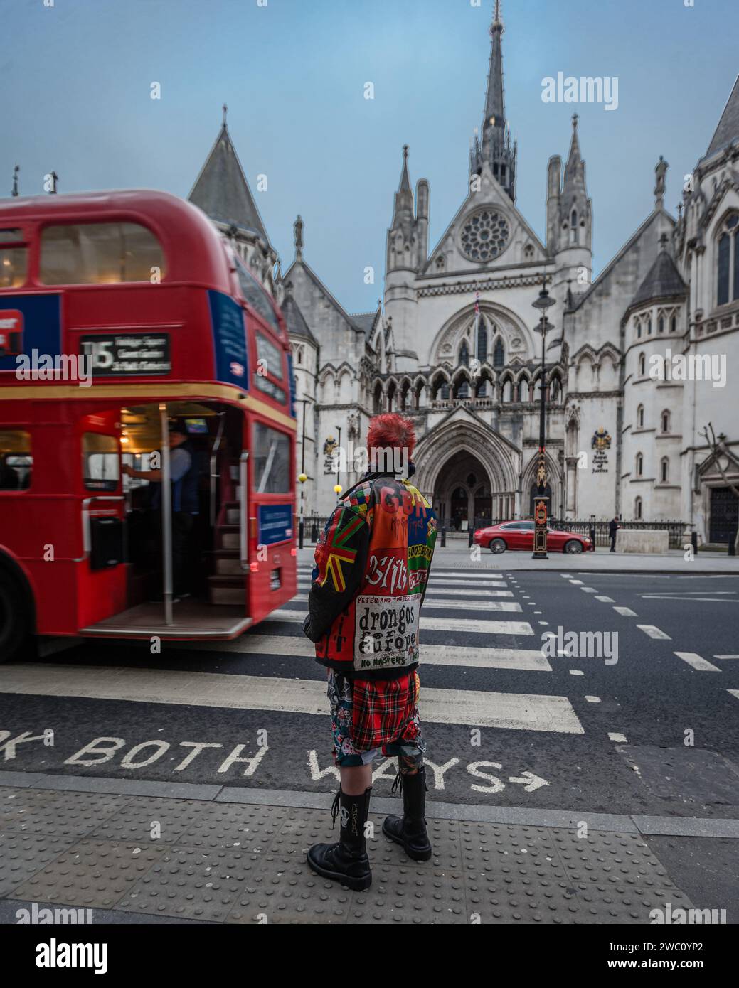 Un bus rouge de Londres, une voiture rouge et un vieux punk à Londres devant les cours royales de justice. Banque D'Images