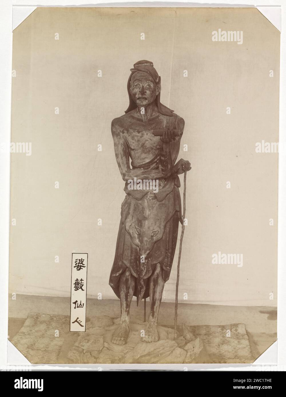 Sculpture du basus immortel dans le temple Sanjusangendo à Kyoto: une figure debout d'un homme maigre avec de longs cheveux, un bâton et un rouleau dans sa main gauche, avec une plaque avec le texte 婆 藪 仙人 仙人 仙人 仙人, 'Basu Sennin à côté de lui sur le sol '(' l'immortel basu '). Basu (Sanskr. Vasu) est représenté comme un ascéet indien ; il apparaît dans les temples bouddhistes japonais comme l'un des assistants de Senju Kannon, le Bodhisattva Avalokiteshvara armé d'un siècle., anonyme, 1890 - 1894 photographie partie de l'album avec 69 photos d'un voyage à travers le Japon. Carton japonais. papier. support photographique imprimé albumine p Banque D'Images