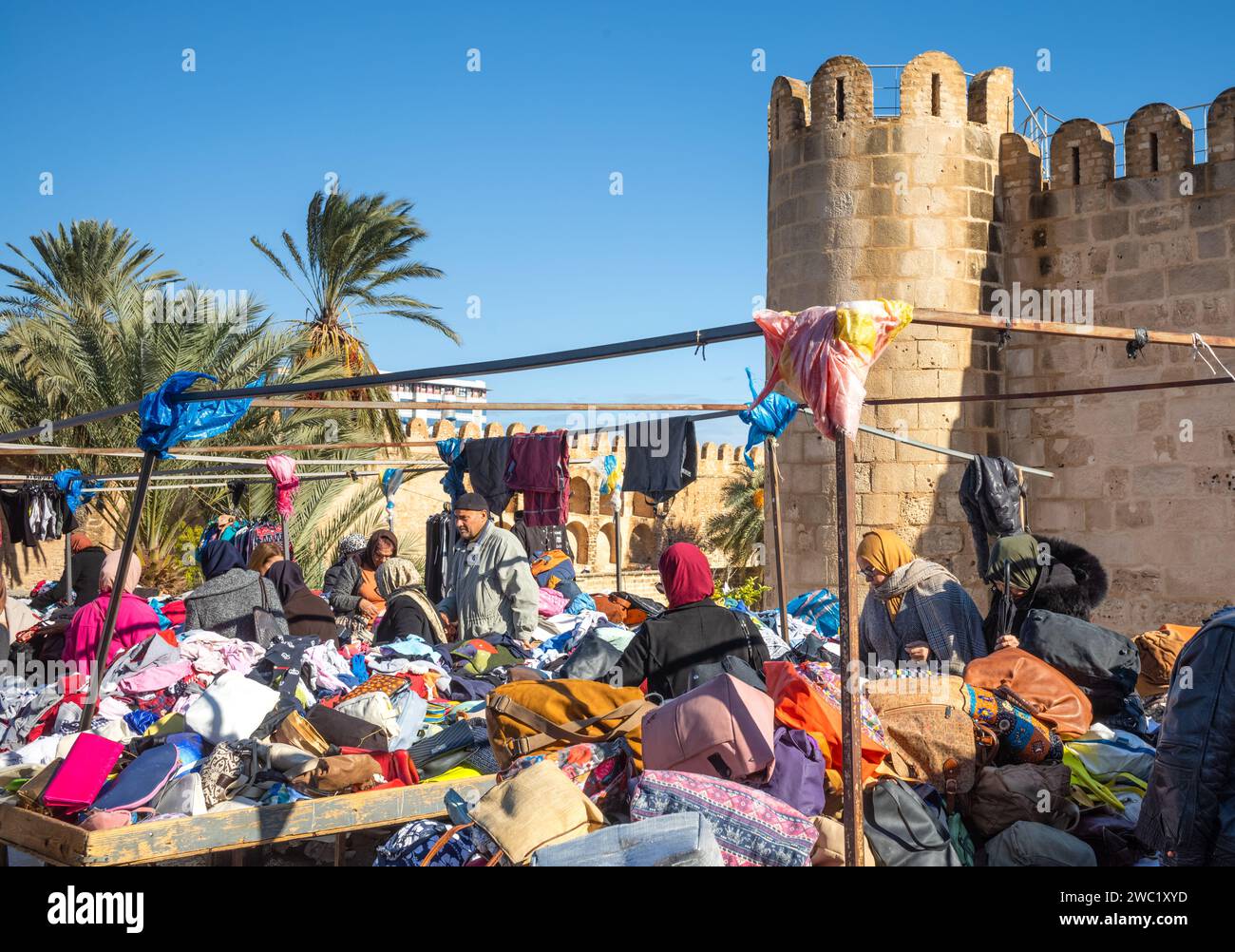 Les gens magasinent dans un marché de vêtements en plein air traditionnel animé à côté du Ribat et des anciens murs de la médina à Sousse, en Tunisie. Banque D'Images