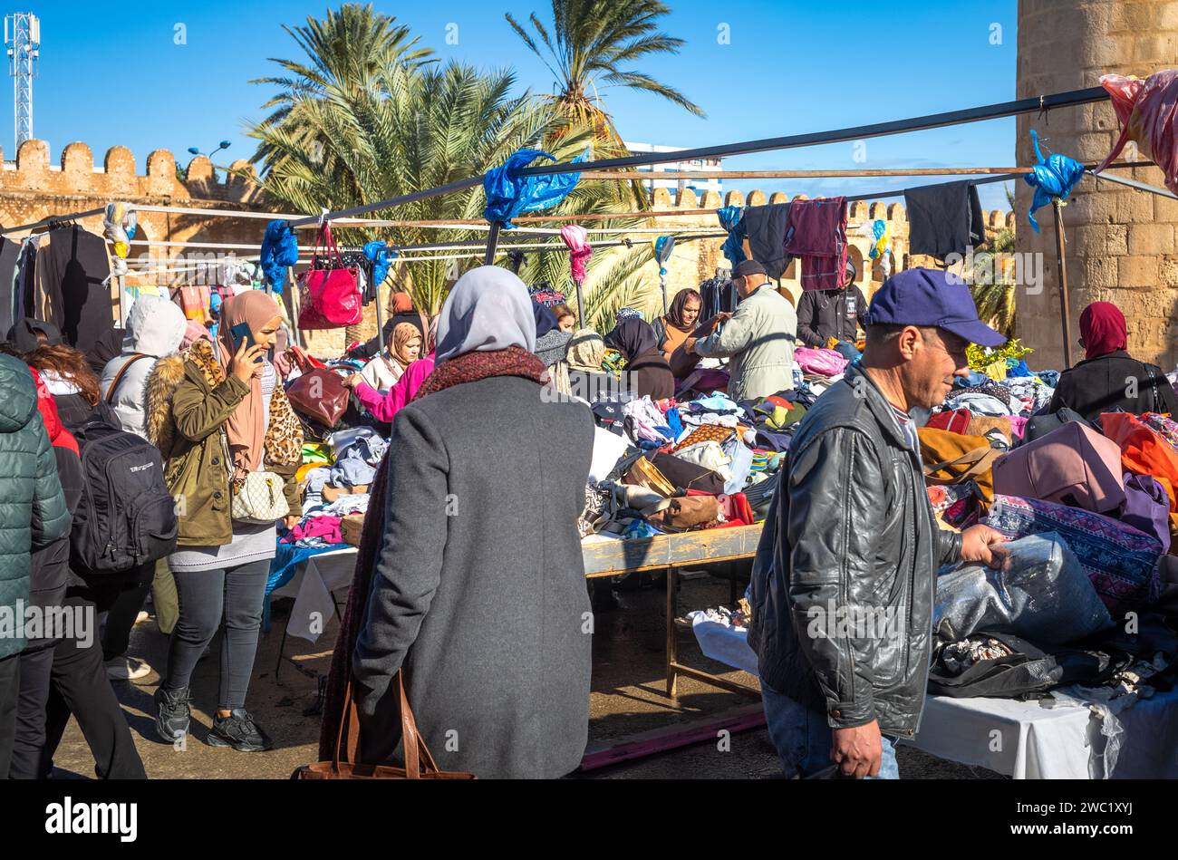 Les gens magasinent dans un marché de vêtements en plein air traditionnel animé à côté du Ribat et des anciens murs de la médina à Sousse, en Tunisie. Banque D'Images