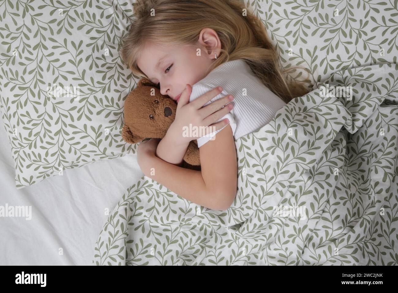 Douce petite fille dormant dans le lit et serrant son ours en peluche Banque D'Images