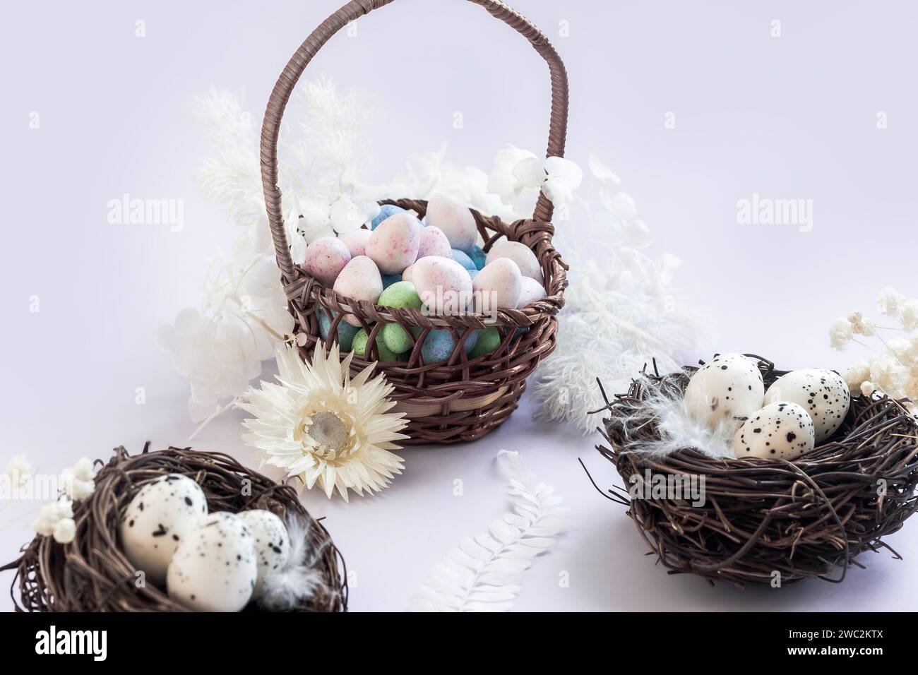 Oeufs en chocolat dans un panier entouré de fleurs séchées et nids d'oiseaux sur fond lilas Banque D'Images