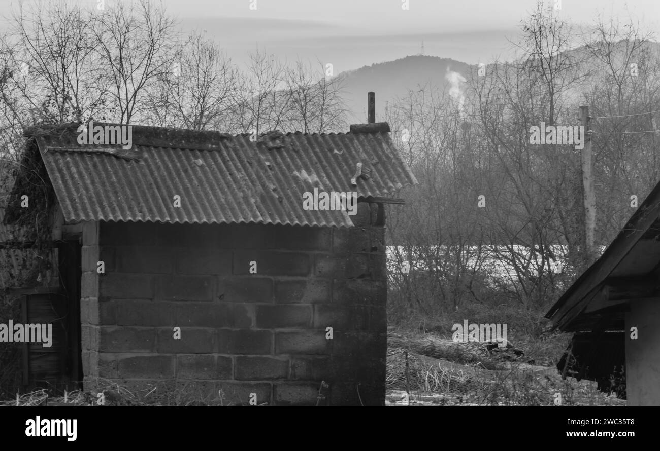 Noir et blanc de petit bâtiment de stockage de gazon en milieu rural avec le soleil rebondissant sur l'atmosphère et la fumée de cheminée en arrière-plan Banque D'Images