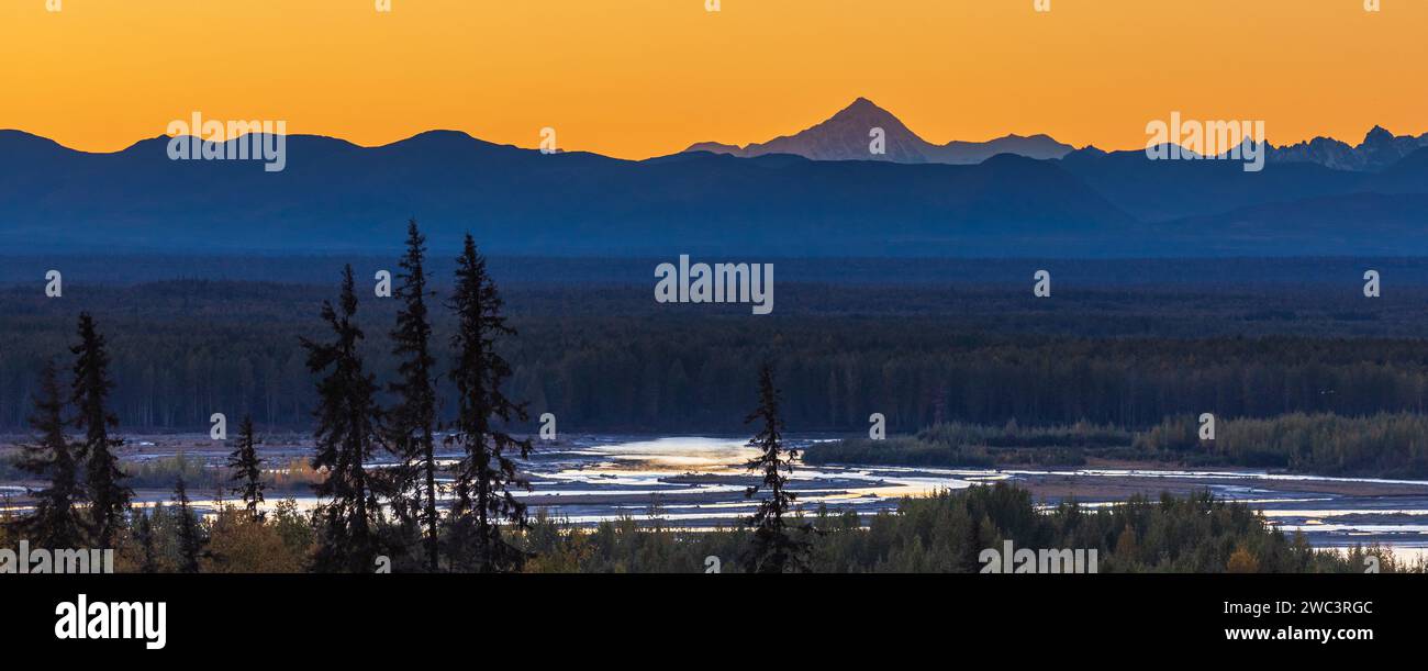 Vue panoramique de la chaîne de montagnes dentelées de l'Alaska dans la lumière crépusculaire du coucher du soleil avec rivière et forêt au premier plan Banque D'Images