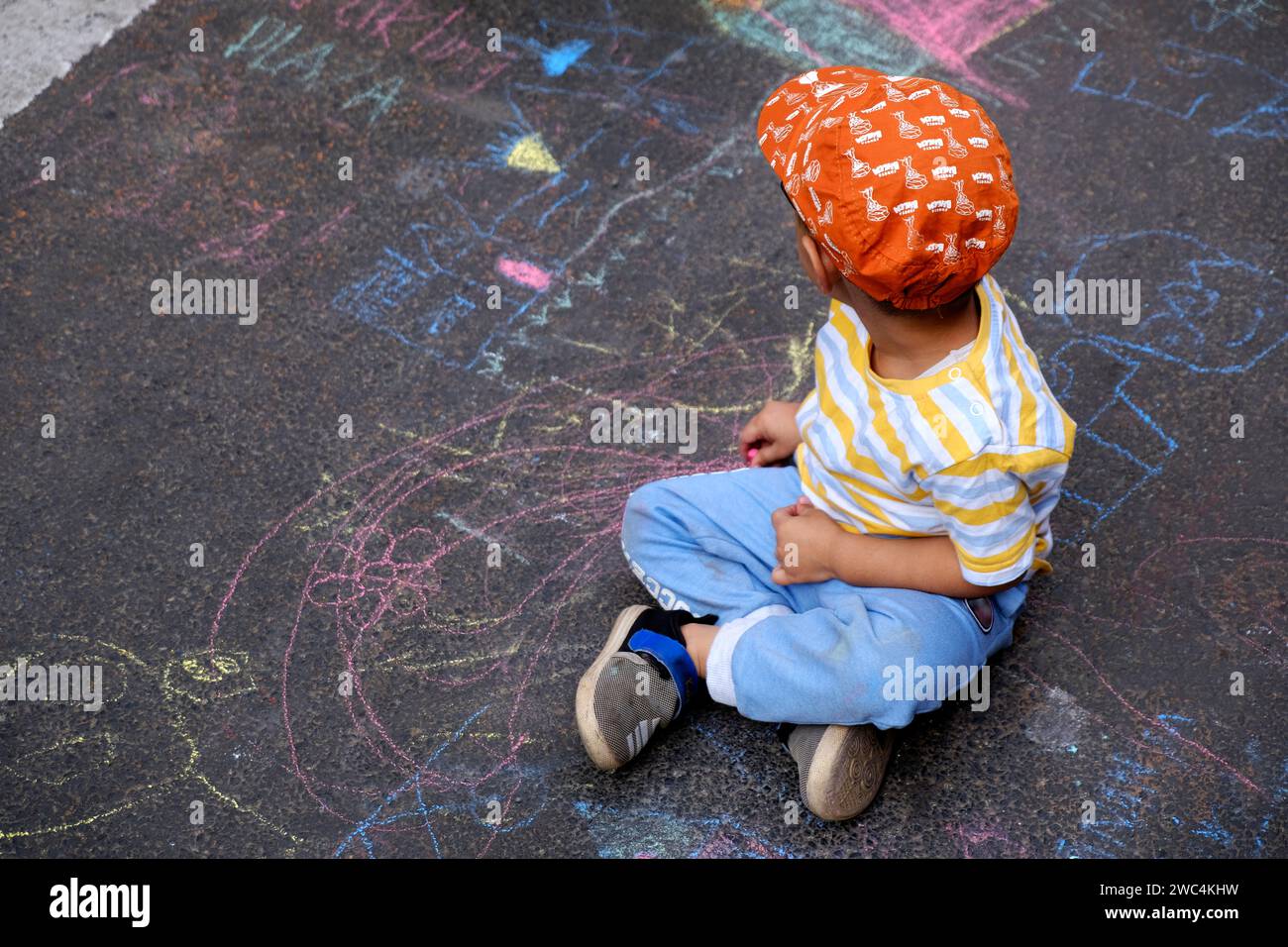 Petit garçon indien dessinant à la craie à l'extérieur. Image des enfants, créativité sur la route grise de dackground, activités extérieures pour les enfants. vue de dessus. Banque D'Images