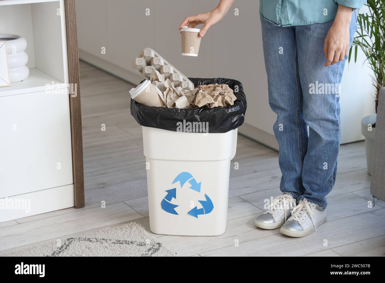 Femme jetant tasse de papier dans la poubelle pleine avec logo de recyclage dans la cuisine Banque D'Images