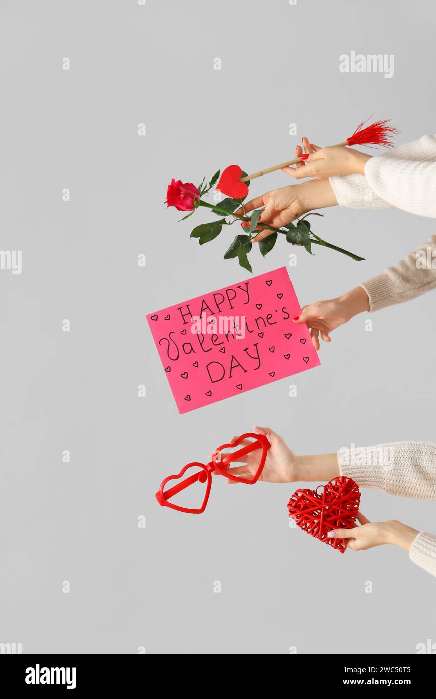 Mains féminines tenant le signe avec le texte HAPPY VALENTINE'S DAY et différents cadeaux sur fond blanc Banque D'Images