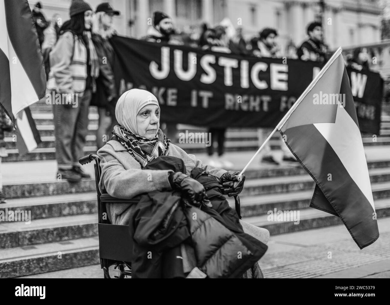 Une vieille dame en fauteuil roulant proteste devant une énorme bannière "JUSTICE NOW Make it Right for Palestine" à Trafalgar Square. Banque D'Images