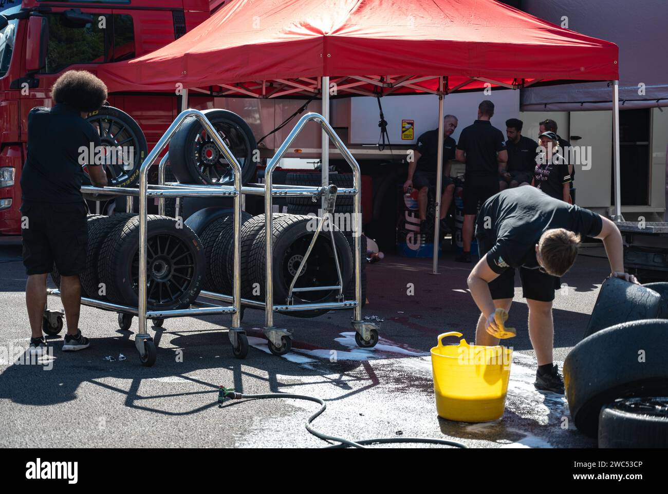 Un garçon nettoie des pneus de course glissants avec une éponge, du savon et de l'eau. Un autre garçon met les pneus de pluie sur les étagères Banque D'Images