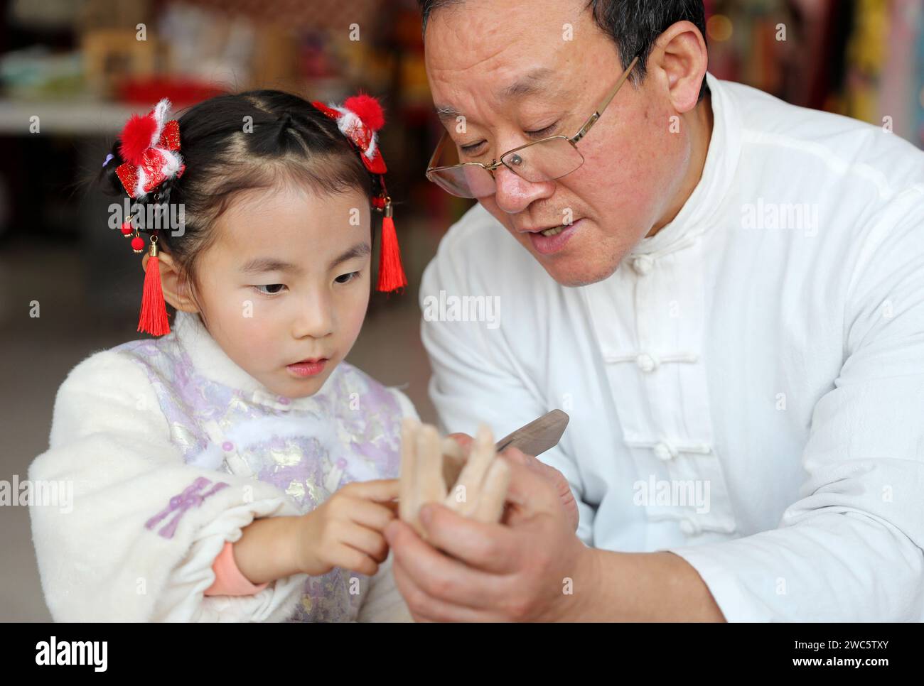 LAIXI, CHINE - 14 JANVIER 2024 - Jiang Yutao, un héritier de spectacles de marionnettes, montre une technique de fabrication de marionnettes à un enfant de Laixi, province du Shandong, en Chine, Banque D'Images