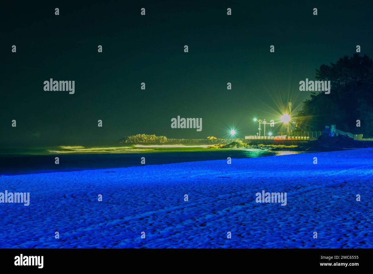 Scène de nuit à la plage lumière bleue douce avec jetée éclairée par des lampadaires en arrière-plan Banque D'Images