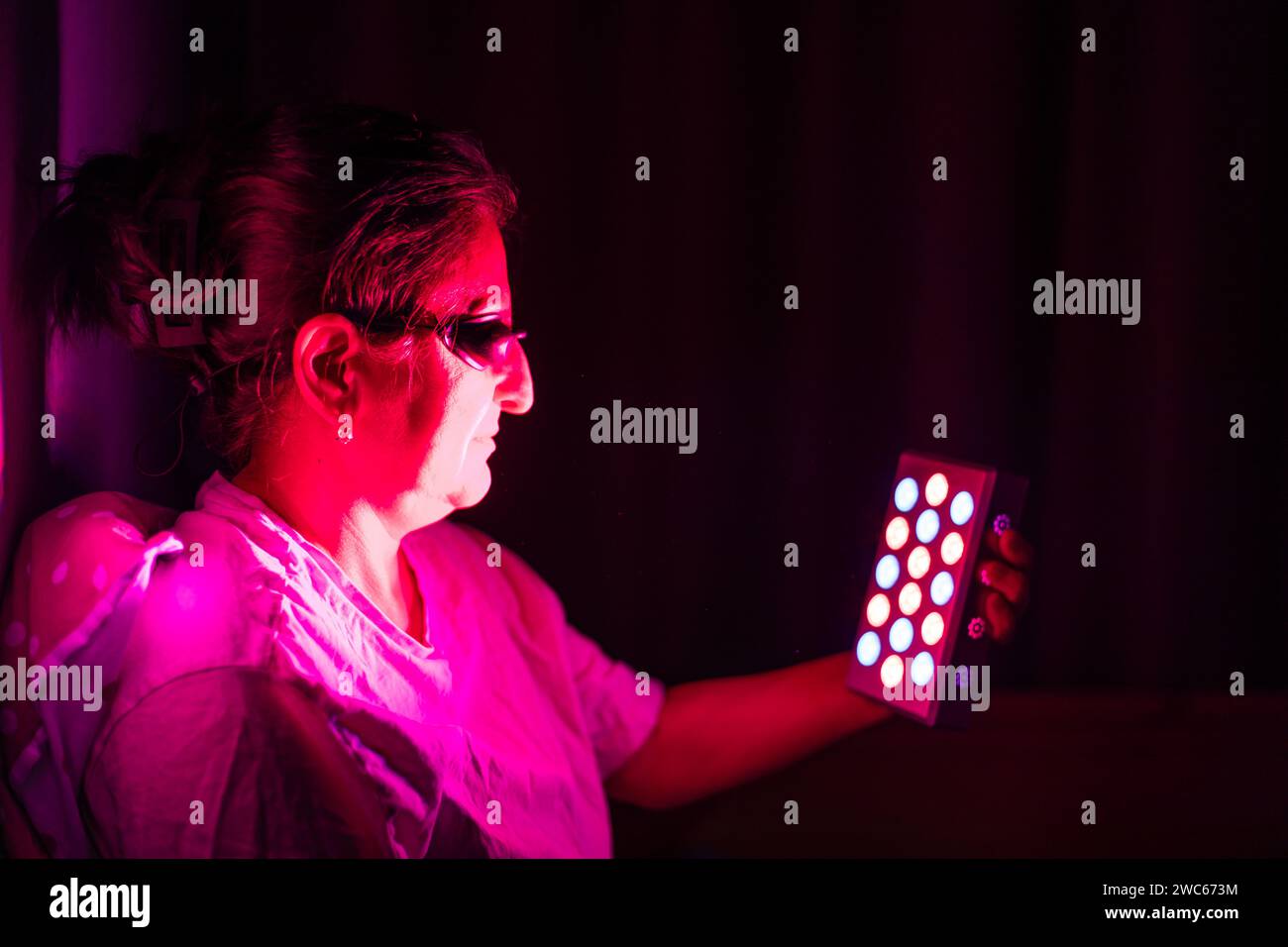 Gros plan d'une femme âgée faisant la séance de thérapie à la lumière rouge avec un appareil portatif et portant une protection oculaire à la maison sur le lit Banque D'Images