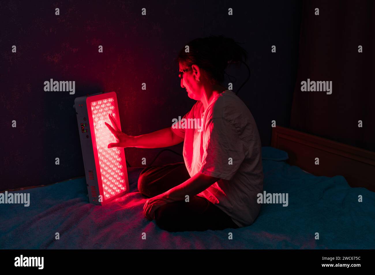 Femme senior touchant les LED du panneau de thérapie de lumière rouge avec la main Banque D'Images