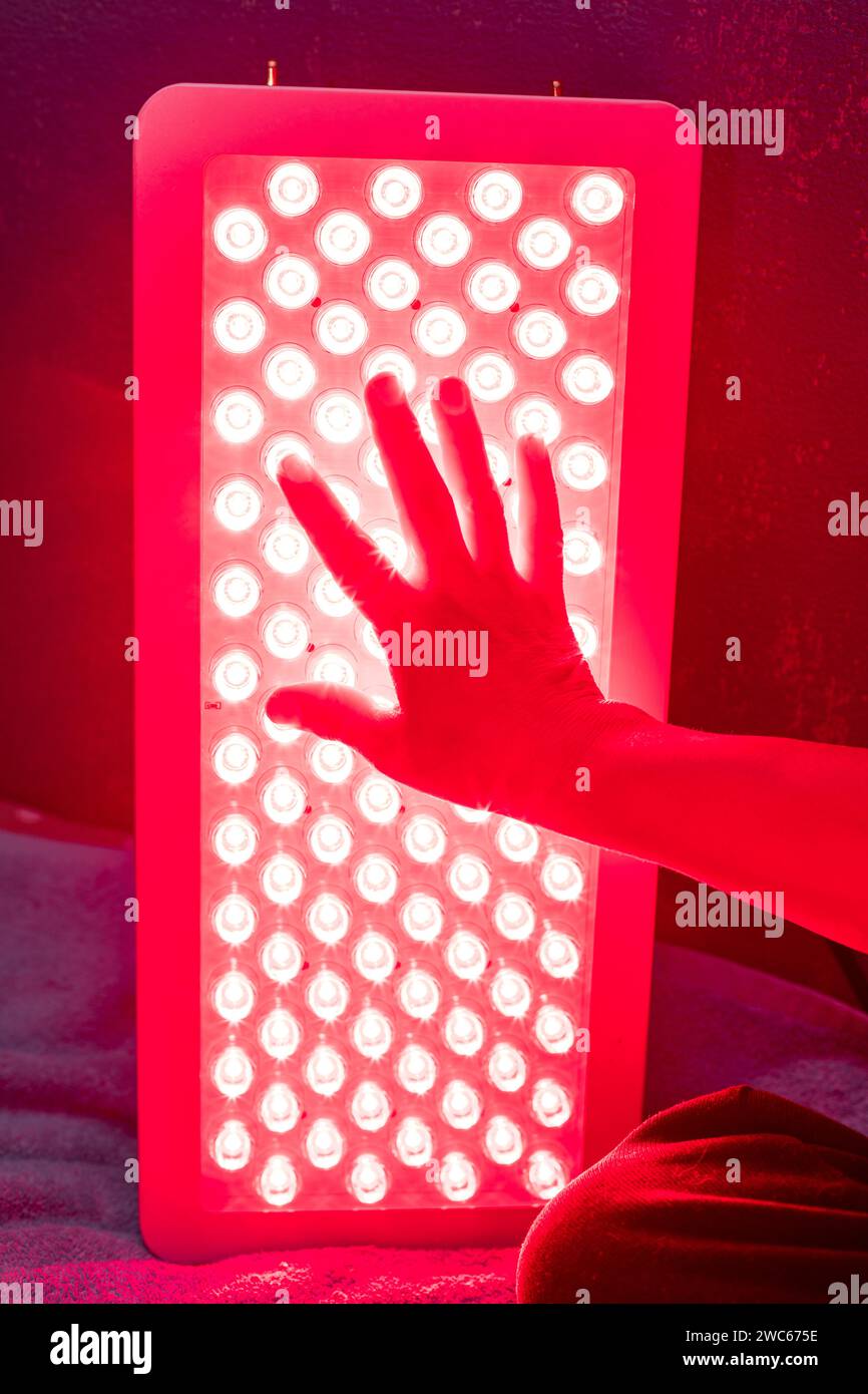 Gros plan de la main touchant les voyants du panneau de luminothérapie rouge Banque D'Images