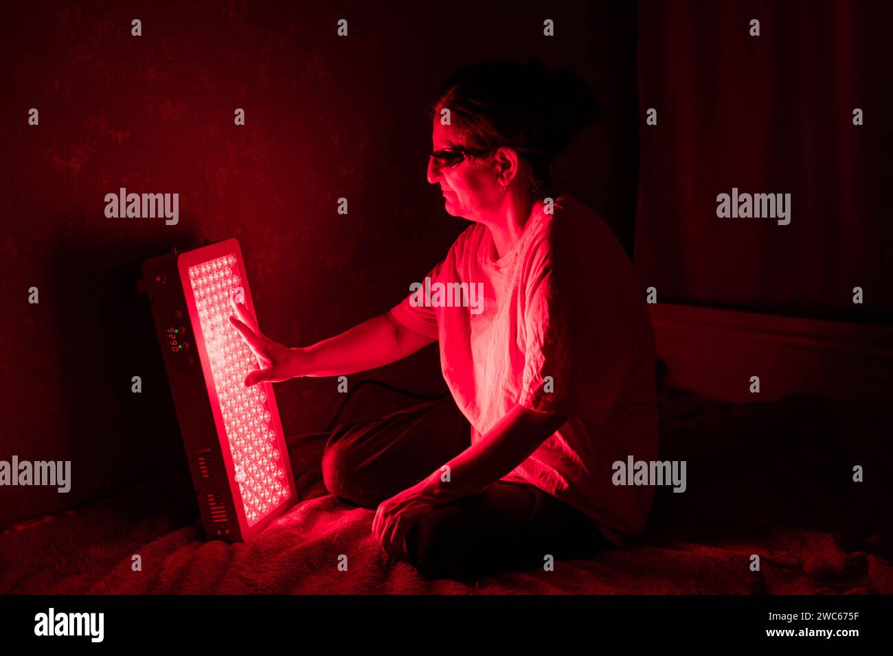 Femme senior touchant les LED du panneau de thérapie de lumière rouge avec la main Banque D'Images