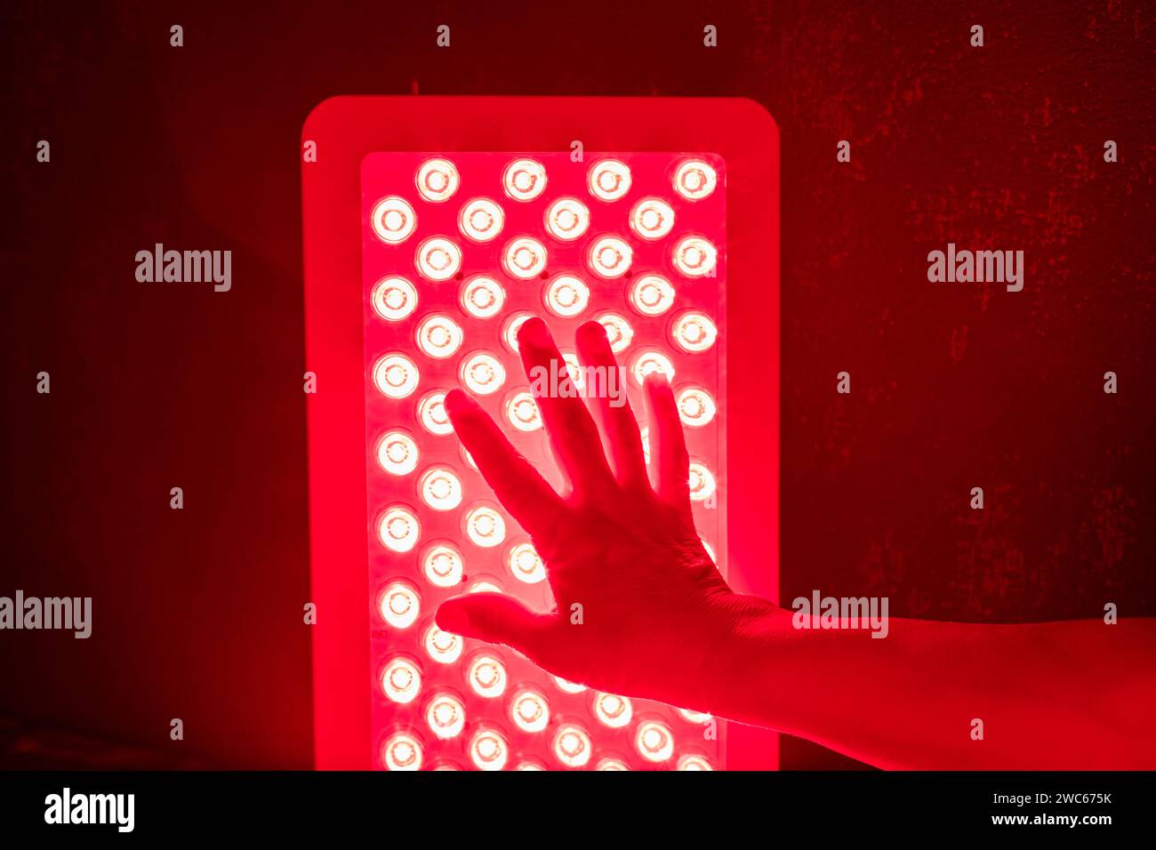 Gros plan de la main touchant les voyants du panneau de luminothérapie rouge Banque D'Images