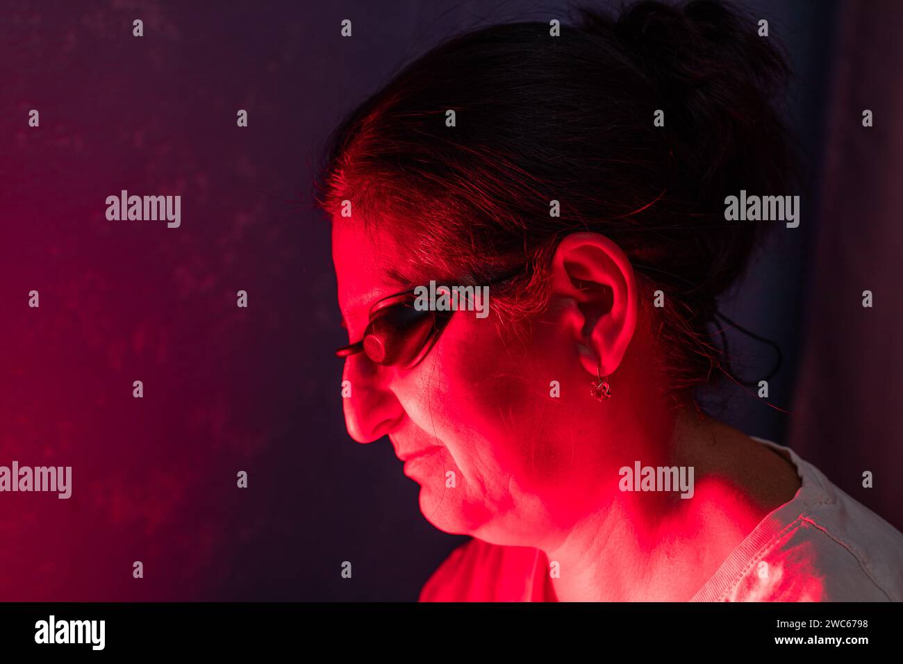 Gros plan du visage de femme senior faisant la séance de thérapie à la lumière rouge avec panneau et portant une protection oculaire Banque D'Images